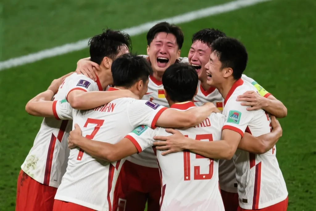 一群身穿国家队战袍的球员在绿茵场上紧紧拥抱,脸上洋溢着激动的泪水与笑容,展现无与伦比的团队凝聚力